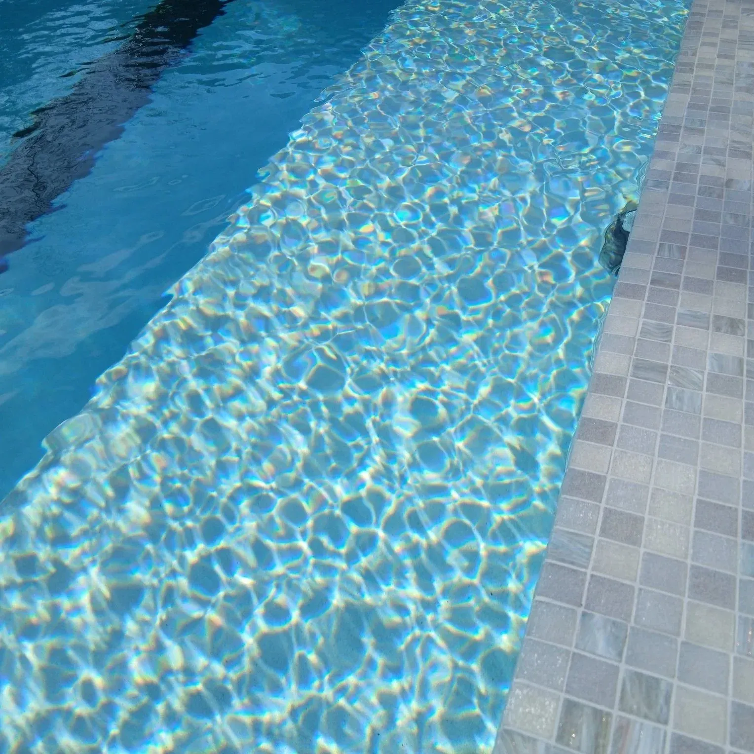 Sunlit pool water beside a mosaic-tiled edge.