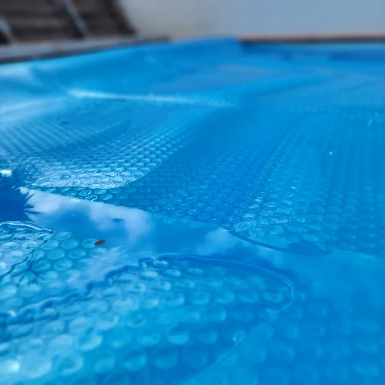 A blue bubble pool cover floating on the water.