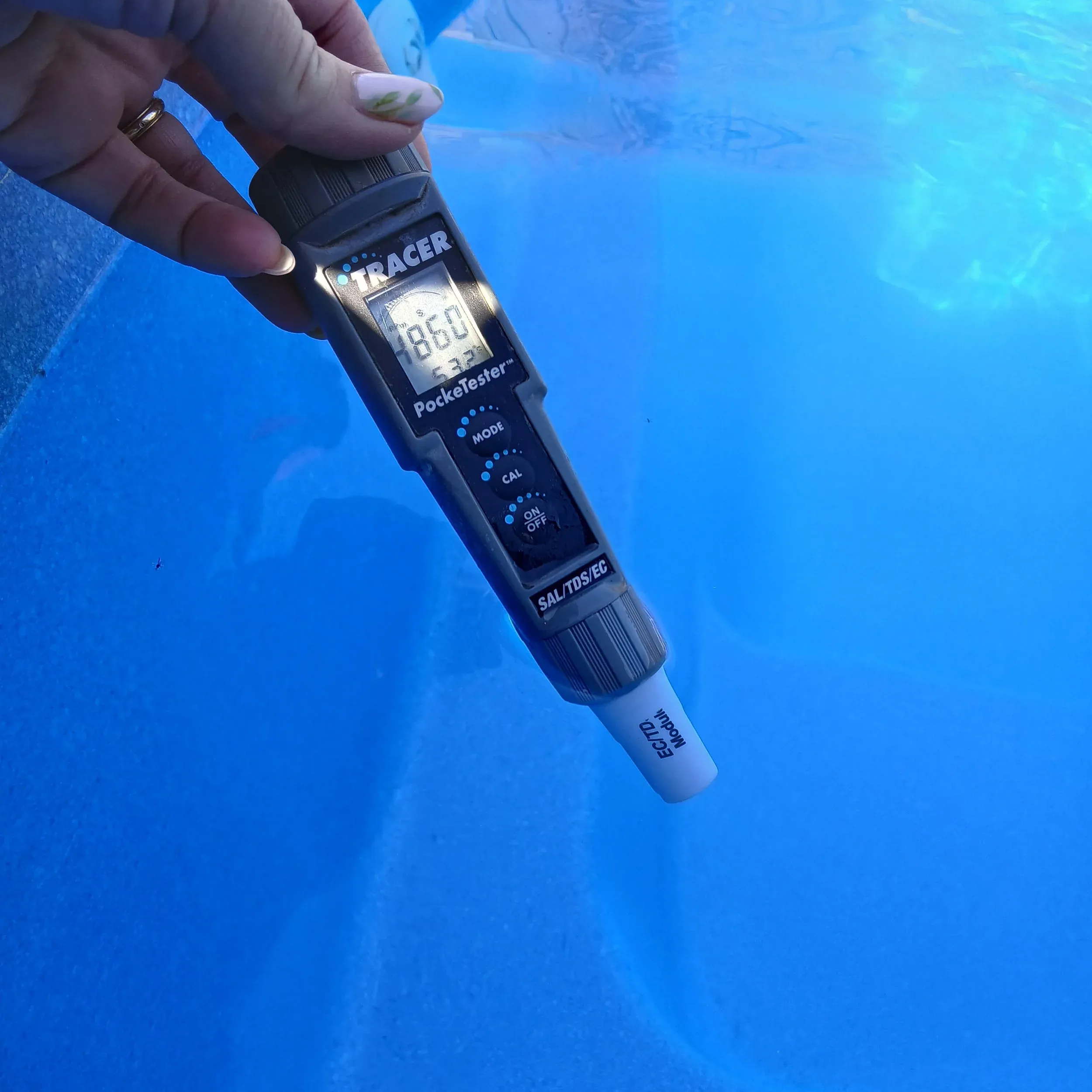 A digital water tester held over clear blue pool water.